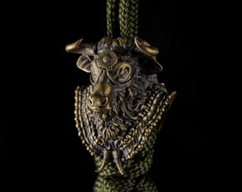 May include: A bronze-colored bull pendant with intricate detailing, including horns, a floral design on the forehead, and a decorative collar. The pendant is suspended from a green braided cord, set against a black background.