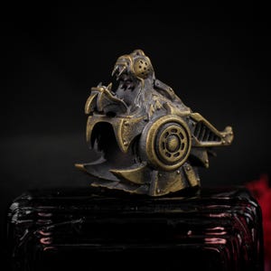 May include: A detailed, steampunk-style metal sculpture of a lion's head. The sculpture features intricate mechanical details, rivets, and a weathered bronze and black finish. The lion's mouth is open, revealing sharp teeth.