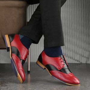 May include: A pair of red and black leather oxford shoes featuring classic brogue detailing, a lace-up closure, and a stacked heel with a purple and tan sole. The shoes are worn with dark blue socks and black plaid trousers.