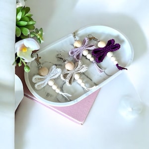 May include: Four crocheted dragonfly keychains with wooden beads. The dragonflies are in shades of purple, lavender, and white.