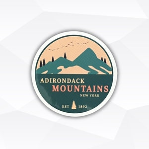 May include: Round sticker with a teal and tan mountain design. The text "ADIRONDACK MOUNTAINS NEW YORK" is in the center, with "EST 1892" at the bottom. The sticker has a white border and a glossy finish.