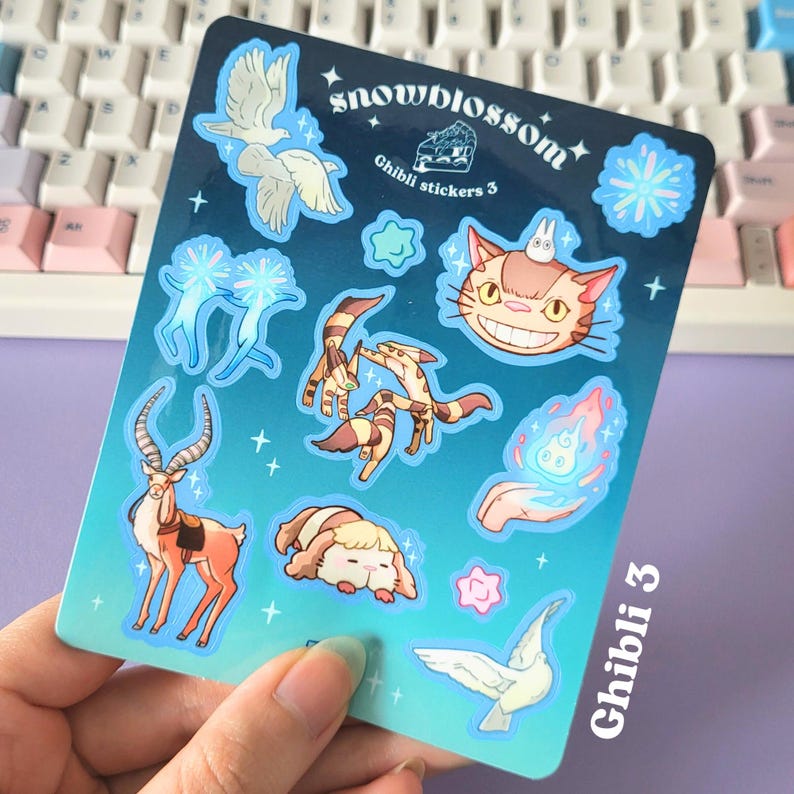 May include: A sheet of stickers featuring characters from Studio Ghibli films. The stickers are on a blue background with white stars and glitter. The stickers include Totoro, the Catbus, Kiki's Delivery Service, and more. The sheet is labeled "Snowblossom Ghibli Stickers 3".