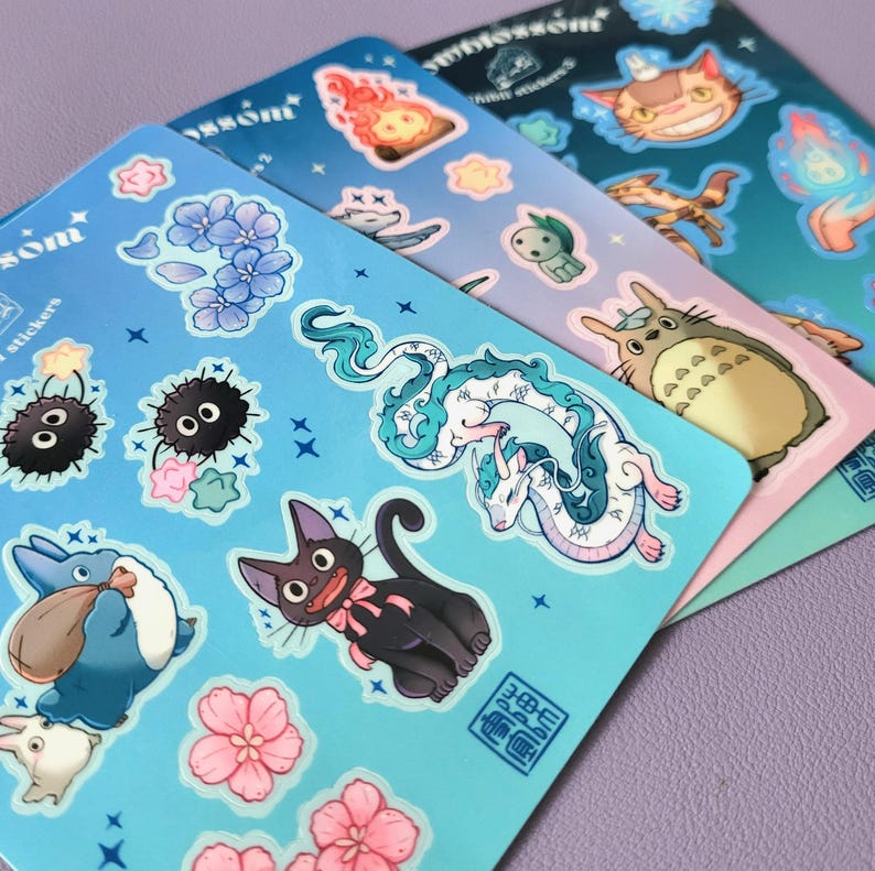 May include: A set of blue, pink, and green sticker sheets featuring characters from the animated film My Neighbor Totoro. The stickers include Totoro, the Catbus, and other characters from the film. The stickers are printed with a glossy finish and have a whimsical, cartoon style.