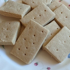 May include: A plate of plain, rectangular shortbread cookies. The cookies are stacked on top of each other and have a light brown color.