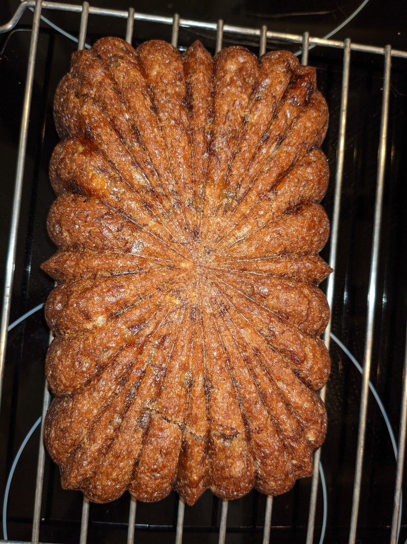 May include: A golden brown banana bread loaf with a starburst pattern on top, baked and cooling on a wire rack.