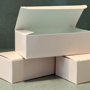 May include: Three pink cardboard boxes, one with the lid open, stacked on top of each other.