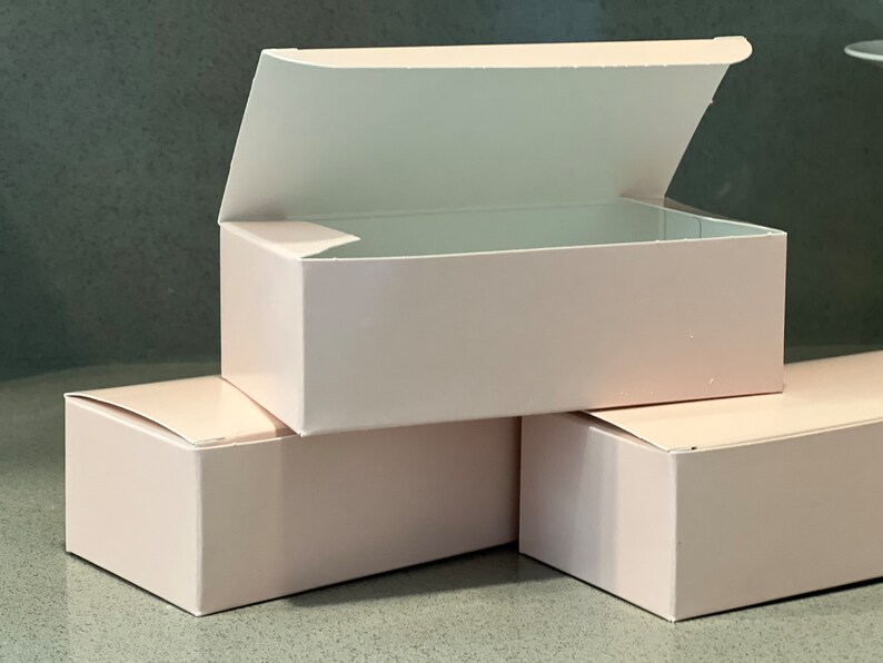 May include: Three pink cardboard boxes, one with the lid open, stacked on top of each other.