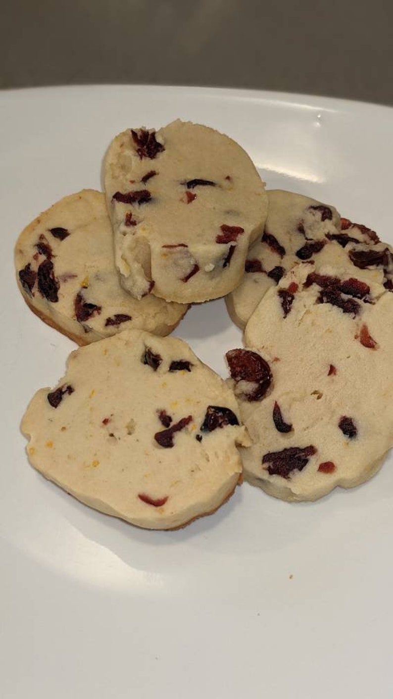 May include: Four shortbread cookies with dried cranberries on a white plate. The cookies are light brown and have a slightly golden hue.