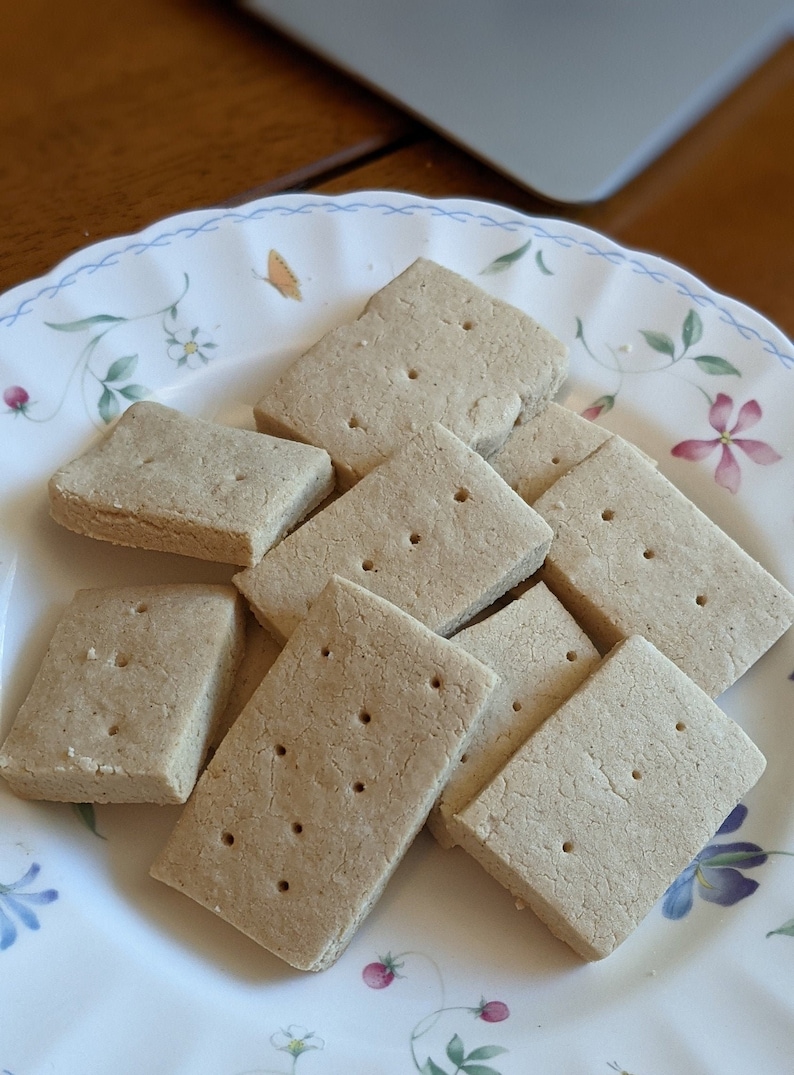 May include: A plate of plain, rectangular shortbread cookies. The cookies are stacked on top of each other and have a light brown color.