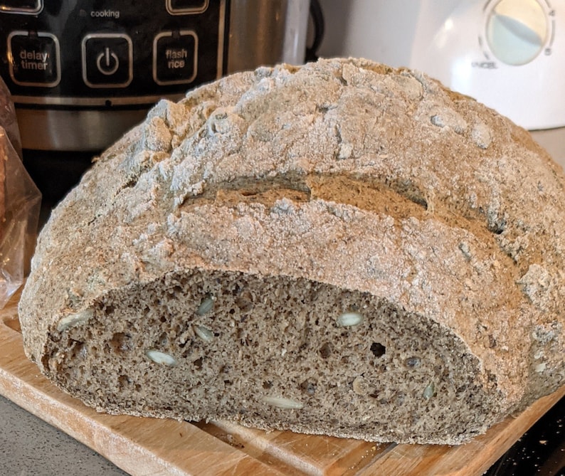 May include: A loaf of freshly baked sourdough bread with a light brown crust and a soft, airy crumb. The bread is sliced in half, revealing a light brown interior with visible seeds.