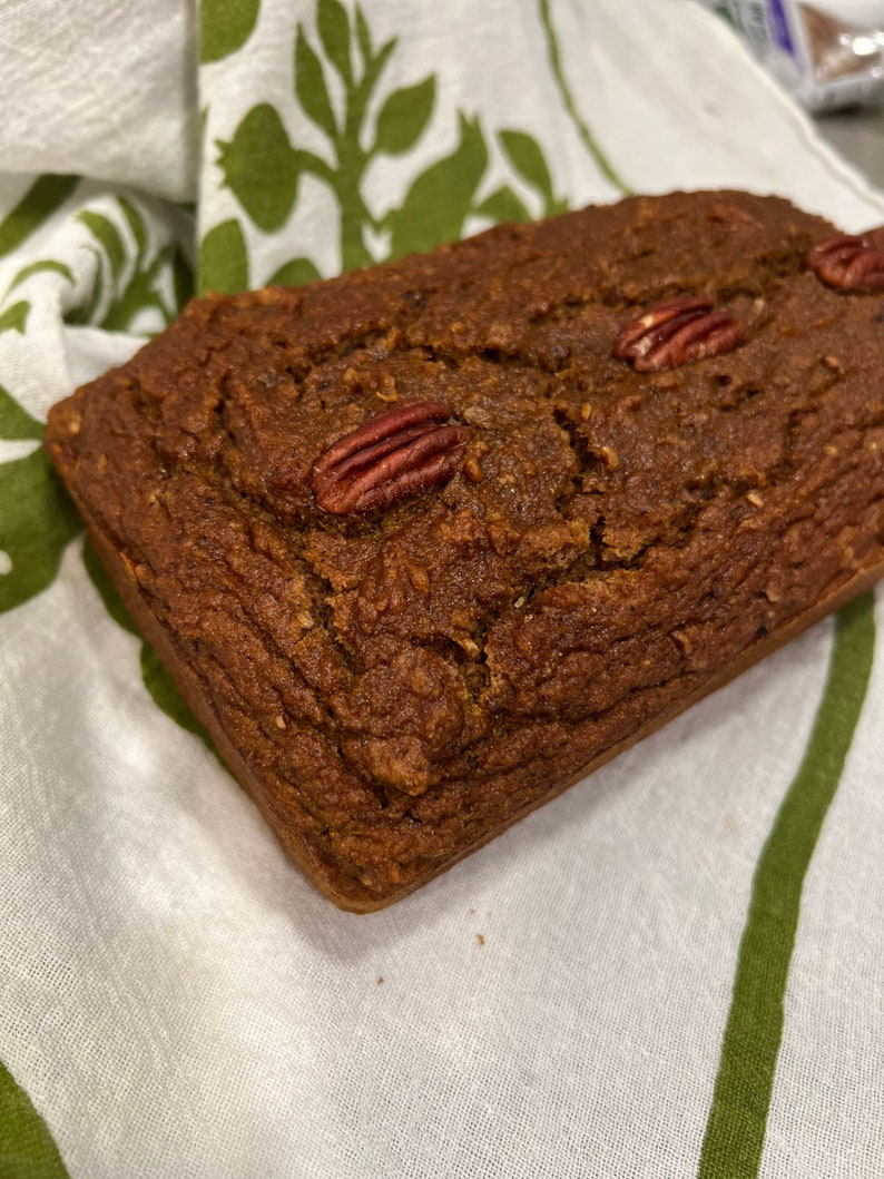 May include: A loaf of pecan bread on a white and green patterned tea towel.