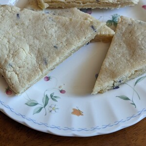 May include: Three triangular pieces of shortbread cookies on a white plate with a floral pattern. The cookies are light brown and have a slightly crumbly texture.