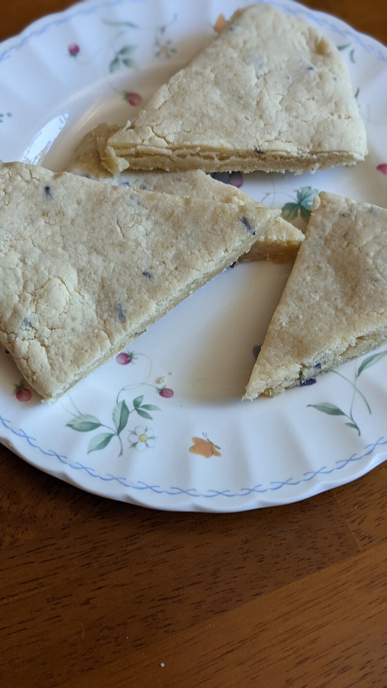 May include: Three triangular pieces of shortbread cookies on a white plate with a floral pattern. The cookies are light brown and have a slightly crumbly texture.