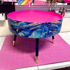 Runt soffbord, blå och guldfärgad marmoreffekt. Marinblå och metallisk effekt. Stark rosa, lyftbar förvaring ovanpå. Sidobord för lounge