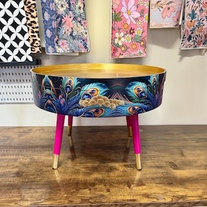 Ronde salontafel, pauwenmotief, blauwe, groenblauwe en turquoise veren. Helderroze en goud, bovenkant eraf halen om op te bergen. Bijzettafel lounge