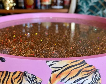 May include: Pink tray with a glittery gold surface and a tiger print design. The tray is round and has a raised edge.