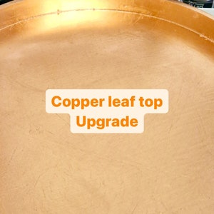 Puede incluir: Primer plano de una superficie redonda de color dorado con el texto "Copper leaf top Upgrade" en naranja.