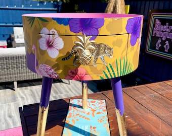 Tavolo da soggiorno rotondo con cassetto. Comodino o tavolino ideale. Design tropicale giallo con piano rosa, gambe viola e foglia oro