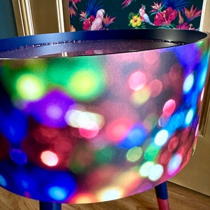 May include: A blue side table with three legs. The table top is covered in a fabric with a blurred out pattern of colorful lights.