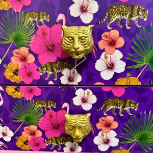 May include: A purple chest of drawers with a tropical design. It features pink hibiscus flowers, green palm leaves, and leopard print accents. The drawer pulls are gold tiger heads.