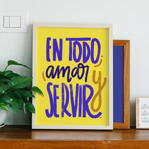 Puede incluir: Una impresión enmarcada amarilla con el texto "EN TODO amar y SERVIR" en letras moradas y doradas.