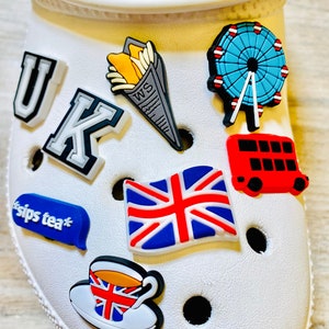 May include: A set of colorful shoe charms featuring UK-themed designs, including a Union Jack flag, a red double-decker bus, a cup of tea, a newspaper-wrapped package of chips, and the letters "UK".
