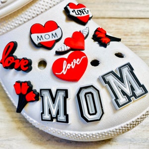 May include: White shoe with red and black heart-shaped charms that say "love" and "mom". There are also charms with red tulips and wings.