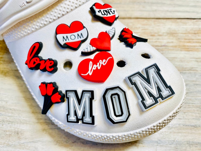 May include: White shoe with red and black heart-shaped charms that say "love" and "mom". There are also charms with red tulips and wings.