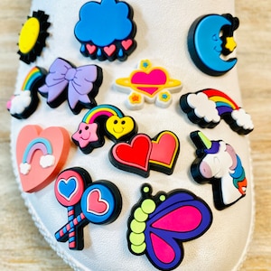 May include: A set of colorful shoe charms featuring various designs, including a rainbow, a heart, a cloud, a butterfly, a unicorn, a star, a lollipop, and a crescent moon.