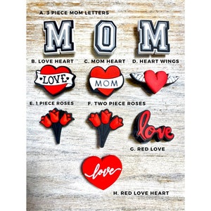 May include: A set of red and white shoe charms with various designs, including the word "MOM", hearts, roses, and the word "love".