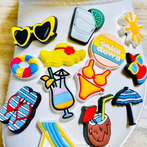 May include: A set of 13 colorful summer-themed shoe charms, including a yellow sun, a blue and white striped umbrella, a yellow and blue beach chair, a yellow and red bikini, a yellow straw hat, a pink and blue life preserver, a blue and white striped flip-flop, a yellow and red cocktail, a brown coconut with a red umbrella and a straw, a yellow and green lime margarita, a pair of yellow sunglasses, and a pink and yellow circle with the text "calm down".