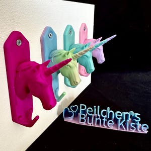 Könnte beinhalten: Ein Set aus fünf Wandhaken in Form von Einhornköpfen in verschiedenen Pastellfarben: Pink, Hellblau, Grün, Türkis und Lavendel. Jeder Haken ist an einer weißen Holzplatte befestigt. Die Haken sind 3D-gedruckt und haben einen Haken unter dem Einhornkopf.