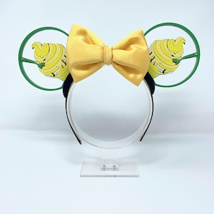 May include: Yellow satin bow headband with green and yellow cartoon ice cream cone ears. The headband is on a clear display stand.