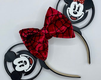 May include: Black and red Mickey Mouse ears headband with a red velvet bow with a spiderweb design. The ears are shaped like Mickey Mouse's head and have a black outline.