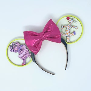 May include: Pink glitter bow headband with yellow and white ears. One ear features a purple and pink character, the other ear features a white and orange character.