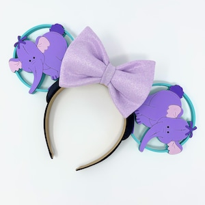 May include: Purple and teal Minnie Mouse ears with a purple bow and a 3D Dumbo design on each ear.