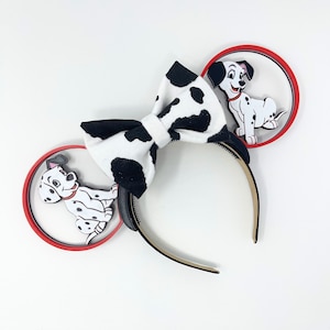 May include: A pair of black and white dalmatian dog ears with red and white headband. The ears are made of fabric and have a bow in the center. The headband is made of plastic and has a red and white pattern.