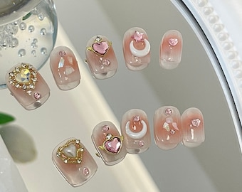 May include: Set of ten pink and white press-on nails with various gold and pink heart and crescent moon designs.