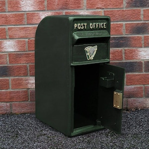 May include: A green metal mailbox with a door that opens to the side. The mailbox has a gold inscription that reads "POST OFFICE" and a gold harp emblem.