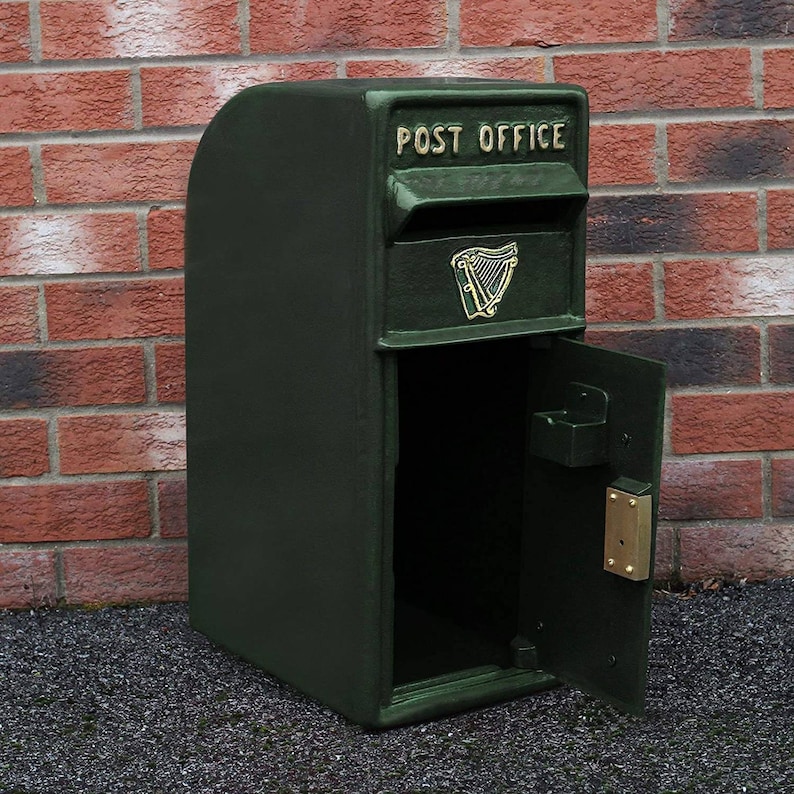 May include: A green metal mailbox with a door that opens to the side. The mailbox has a gold inscription that reads "POST OFFICE" and a gold harp emblem.