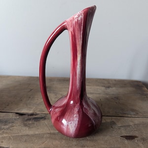 May include: A red and white ceramic vase with a unique curved handle. The vase has a glossy finish and a swirling pattern.