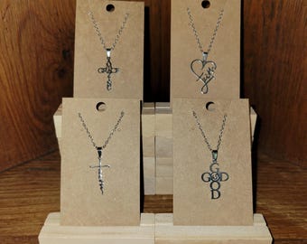 May include: Four silver-toned necklaces displayed on brown cardboard cards. Each necklace has a different cross pendant with words like "Grace", "Faith", and "GOD" inscribed. The necklaces are on a wooden display stand.