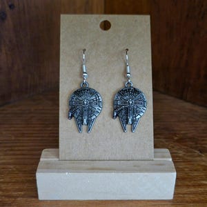 May include: A pair of silver-toned metal drop earrings featuring a detailed, circular spaceship design with intricate mechanical engravings. The earrings hang from standard silver-coloured fishhook wires and are displayed on a rectangular brown card.