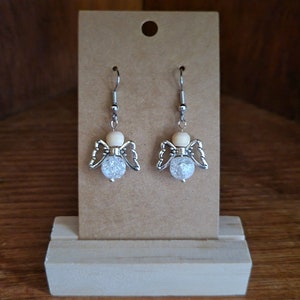 May include: A pair of silver angel wing earrings with clear crystal beads and a wooden bead accent.