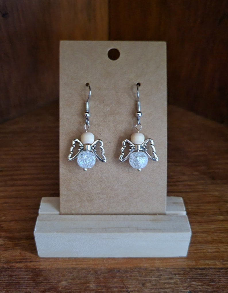 May include: A pair of silver angel wing earrings with clear crystal beads and a wooden bead accent.