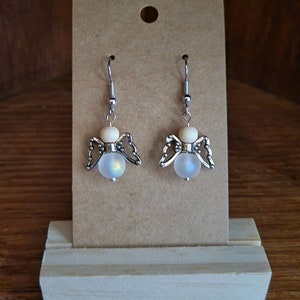 May include: A pair of silver angel-shaped earrings with iridescent white beads and wooden accents.