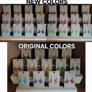 以下が含まれることがあります： 茶色の厚紙にカラフルな手作りイヤリングが並んでいます。イヤリングは風船の動物の形をしています。イヤリングの上段には「NEW COLORS」と表示され、下段には「ORIGINAL COLORS」と表示されています。