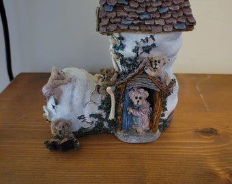 May include: A ceramic figurine of a boot house with a brown roof and a chimney. The boot is white with a brown trim and has several teddy bears peeking out of the windows and door.