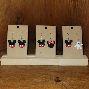 May include: Three pairs of novelty earrings displayed on cardboard stands. The earrings feature black Mickey Mouse heads with red bottoms. One pair has a red bow. Another pair has a white glove design.