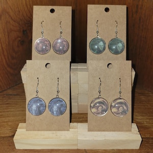 May include: Four pairs of silver-toned dangle earrings. Each earring features a round, artistic image in shades of purple, green, blue, and orange. The earrings are displayed on small, brown cardboard display cards.